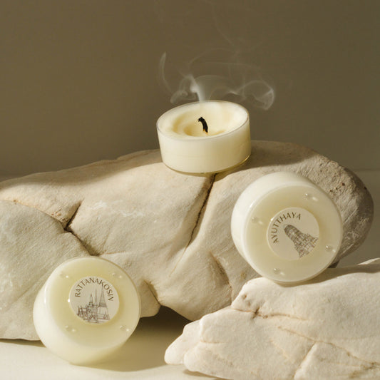 A beige candle with a white label placed on a rock, with a visible wick and smoke rising from the top.