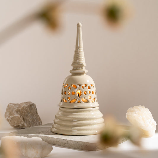 A ceramic candle holder designed in the shape of a Sukhothai-style Stupa with a white color and stencil design, displayed in a bright setting.
